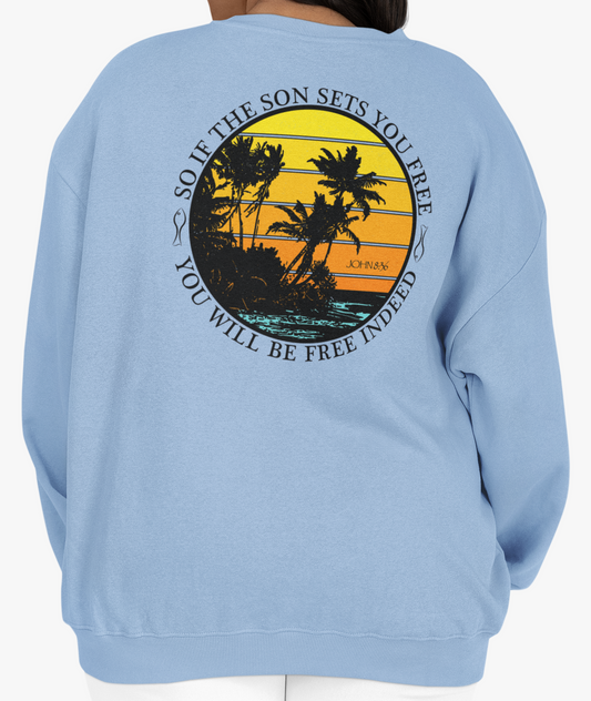 Woman wearing a light blue sweatshirt with a palm tree graphic over a distressed sunset design on the back