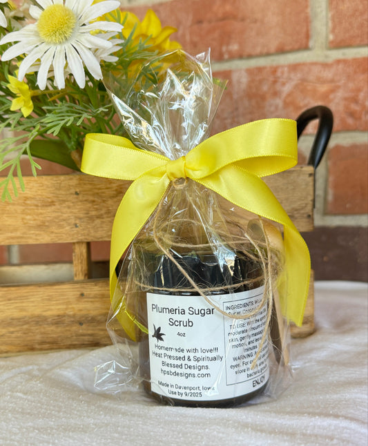 Jar of Sugar Scrub with a yellow ribbon against a brick wall.