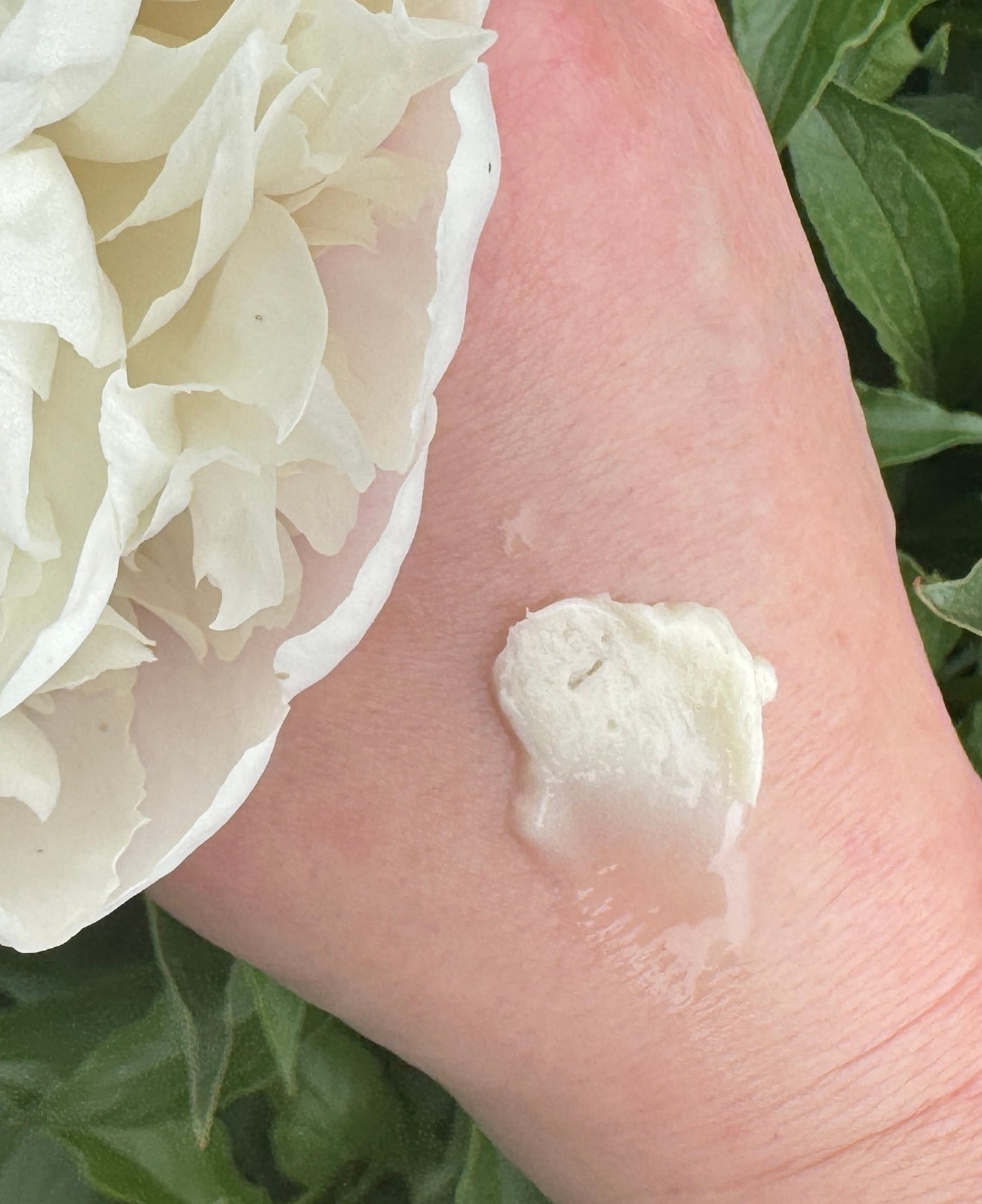 Calendula infused body butter applied to back of hand surrounded by flower and leaves