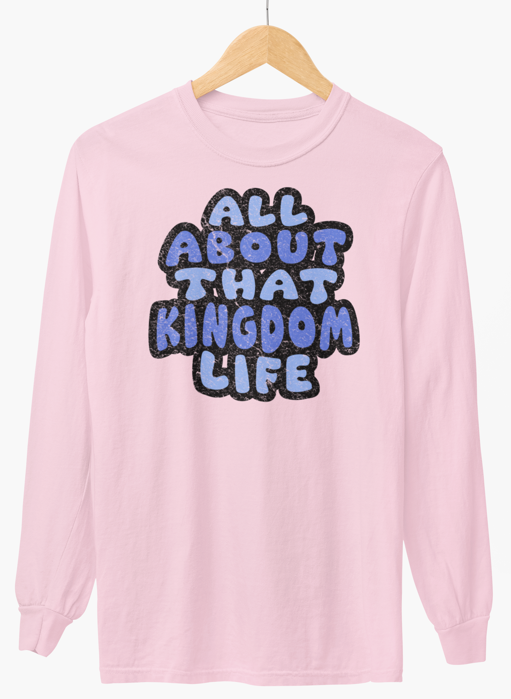 Light pink long-sleeve shirt with 'All About That Kingdom Life' distressed text on a hanger against a white background
