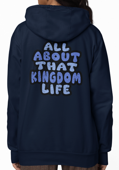 Woman wearing a navy hoodie with 'All About That Kingdom Life' distressed text on the back, standing against a white background.