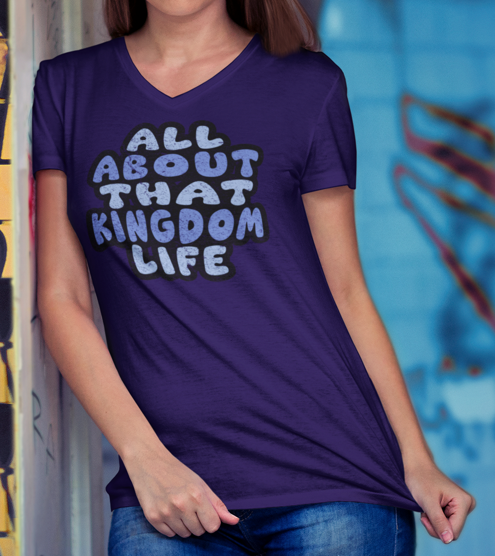 Woman wearing a team purple v-neck t-shirt with distressed text, standing in front of a colorful graffiti wall.