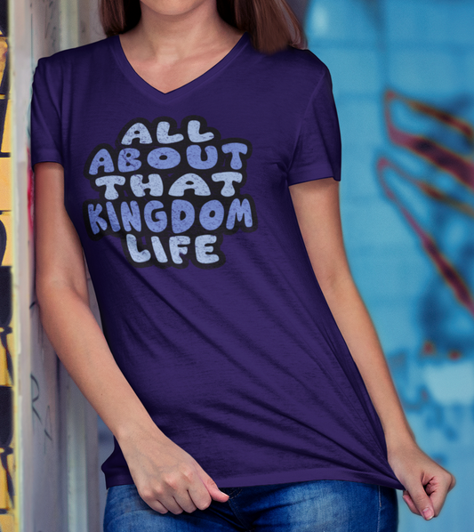 Woman wearing a team purple v-neck t-shirt with distressed text, standing in front of a colorful graffiti wall.