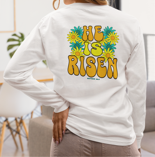 Person wearing a white long-sleeve shirt with 'He is Risen' text and floral design on the back, standing in a living room.