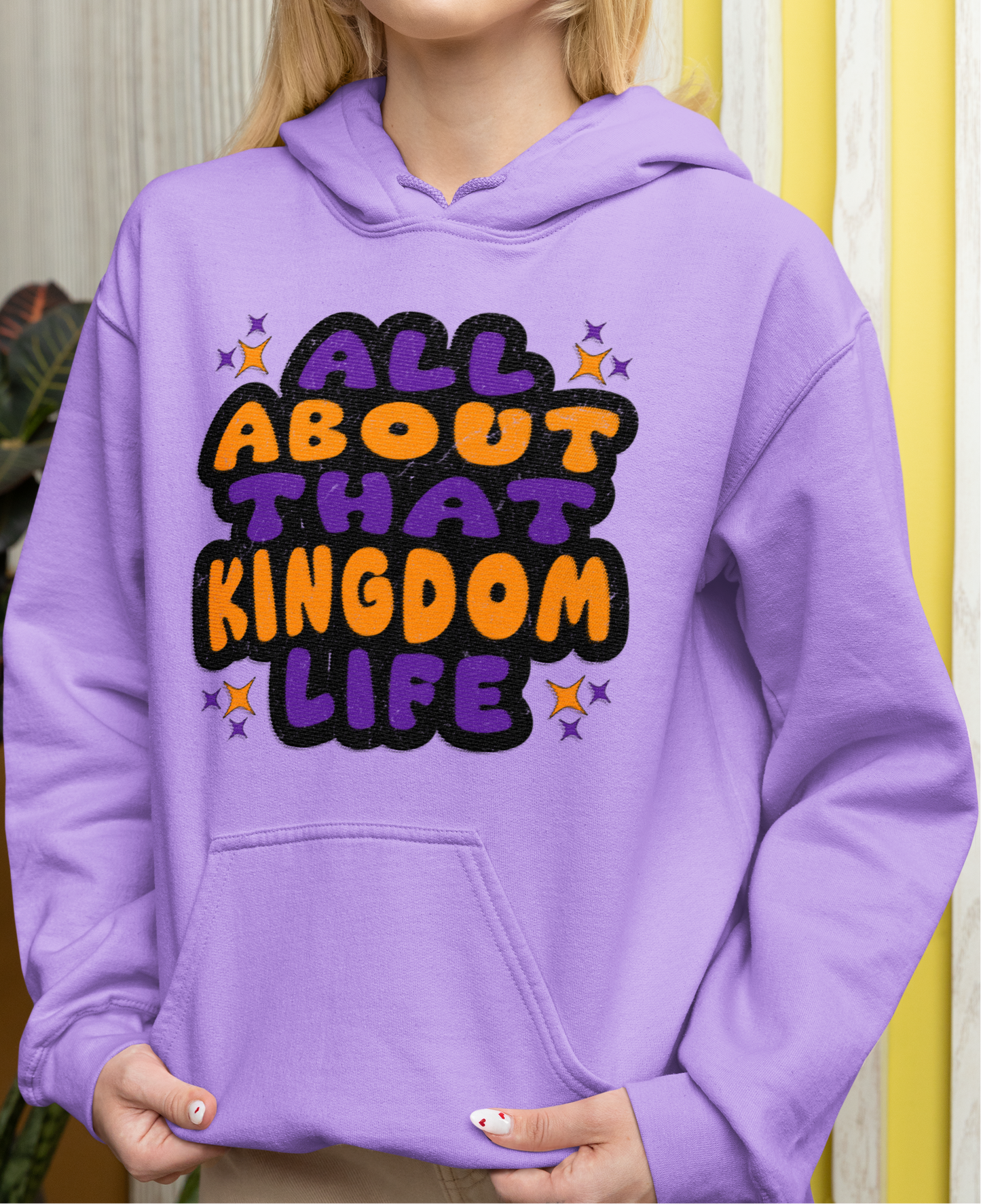 Woman wearing a orchid colored hoodie with 'All About That Kingdom Life' distressed text