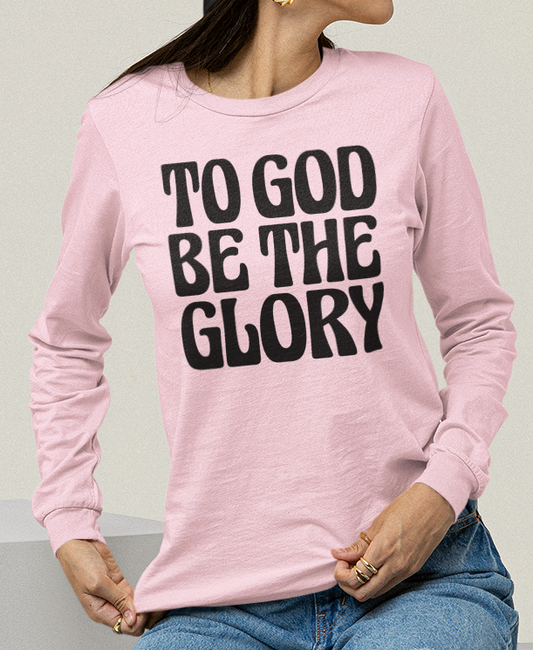 Woman wearing a light pink long-sleeved t-shirt with 'TO GOD BE THE GLORY' black text 